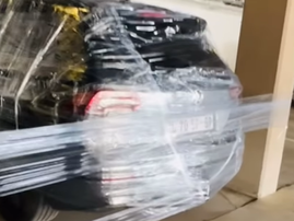 A car is covered in cling wrap parked inside a parking lot