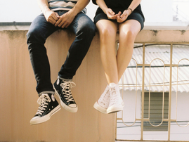 A couple wearing sneakers while sitting next to each other on a wall