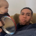 A father looks shocked as his baby hits him with tin biscuit container lid