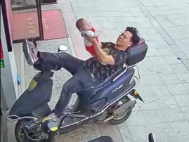 A man leans on his motorbike while holding a baby