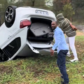 A man looks out as he stands by his overturned car