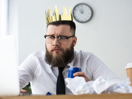 A man wearing a plastic crown sitting in front of his computer at his desk in an office