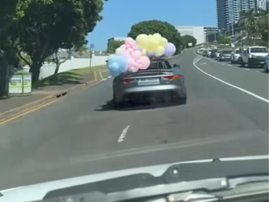 A passenger holds a balloon arrangement out of a convertible car