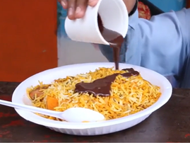 A person pouring chocolate sauce over a plate of biryani