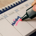 A person writing holiday on a calendar