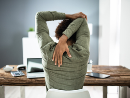 A rear view of a businessman stretching his arms at his desk