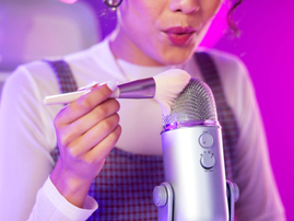 A woman creating ASMR sound on a microphone with a brush