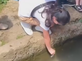 A woman kneels down to swipe her card in a well of water