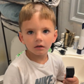 A young boy holding a shaving machine in his hand inside the bathroom