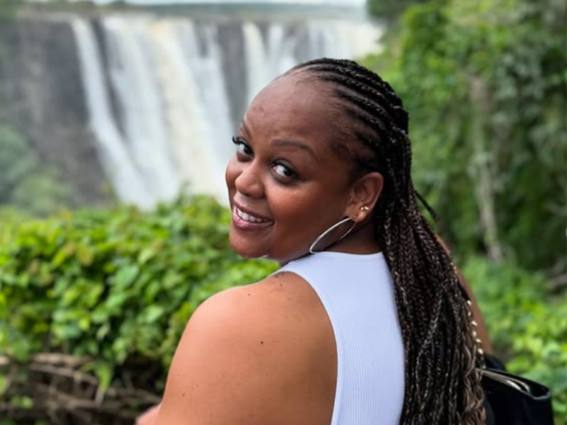 Carol Ofori looking at the camera with the Victoria Falls as her backdrop